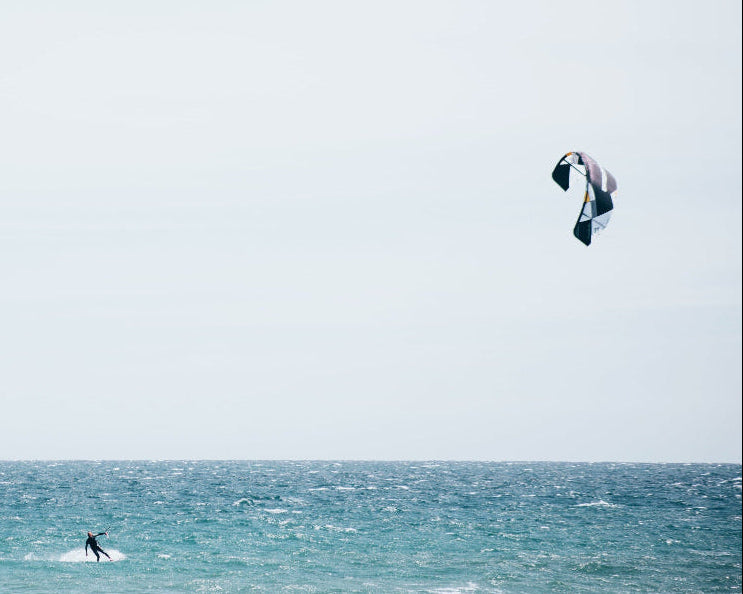Person kite surfing on a vast body of water with a clear sky